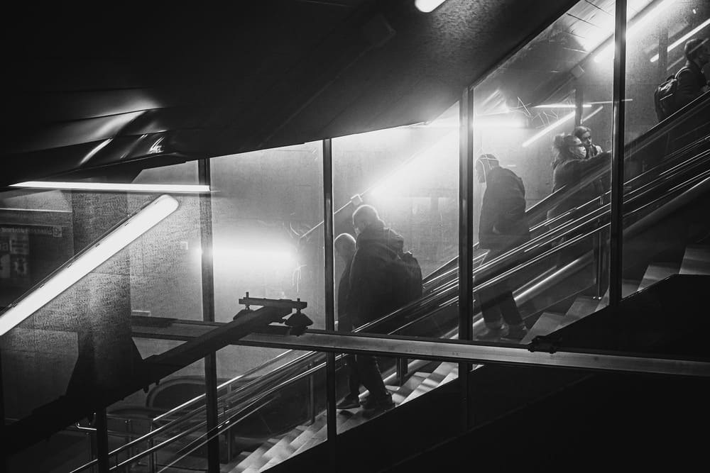 Black and white street photography by Irene Pietrella capturing commuters on an escalator in a modern urban subway station