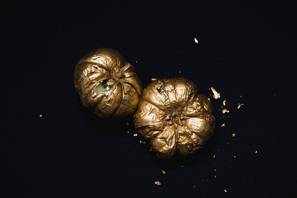Pomodorissimo! Still life art photography by Irene Pietrella featuring two gold-painted tomatoes on a dark background, exploring food and irony