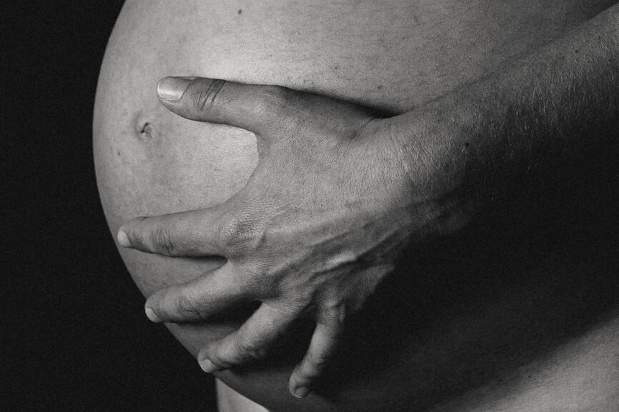 Intimate black and white fine art maternity photograph, close-up of a hand resting on a pregnant belly by Irene Pietrella