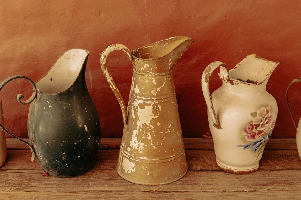 Documentary still life of vintage antique metal pitchers against a textured terracotta wall, photography by Irene Pietrell