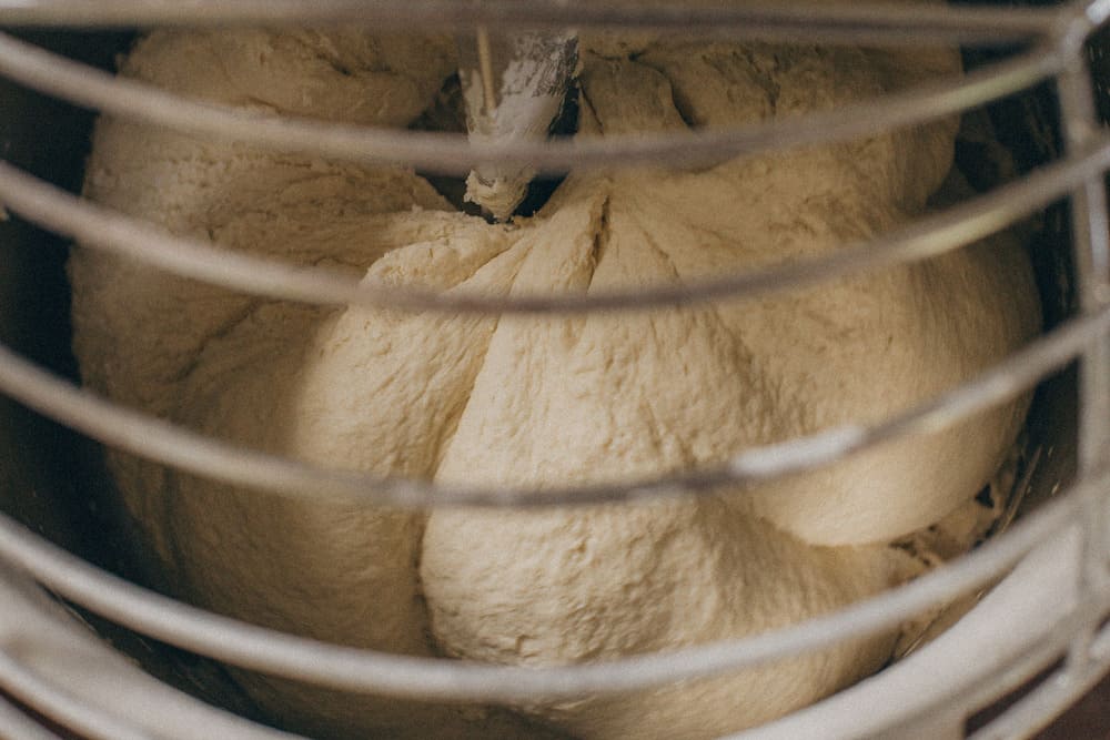 Close-up documentary photography of bread dough being kneaded in an industrial mixer, focus on texture and process by Irene Pietrella
